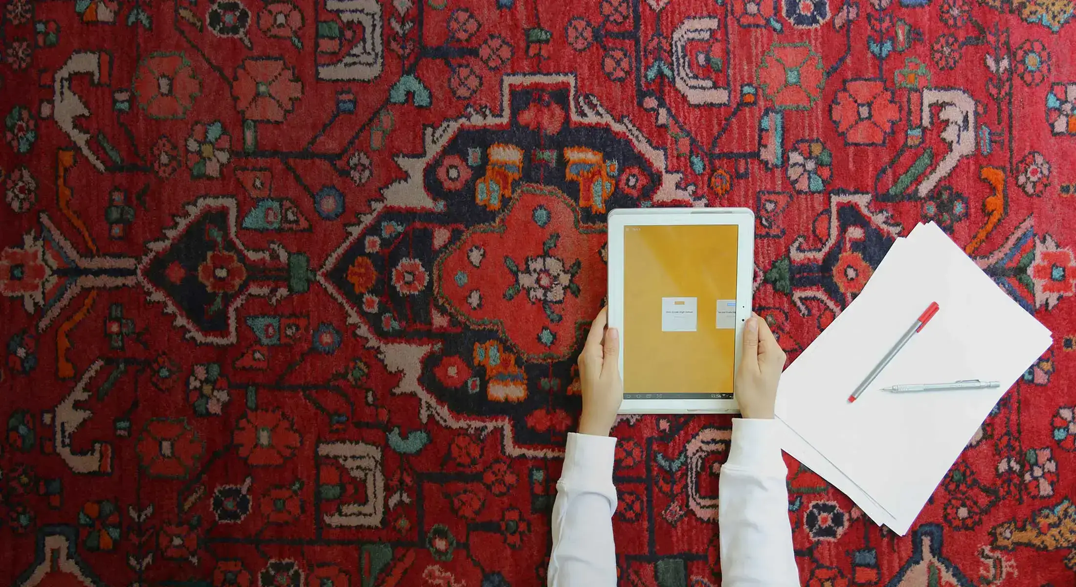 دانش آموزی با اپلیکیشن گاج در تبلت خود بر روی فرش ایرانی کار میکند